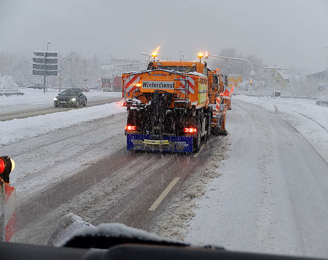 Winterdienstfahrzeug in orange schiebt Schnee von der Straße.