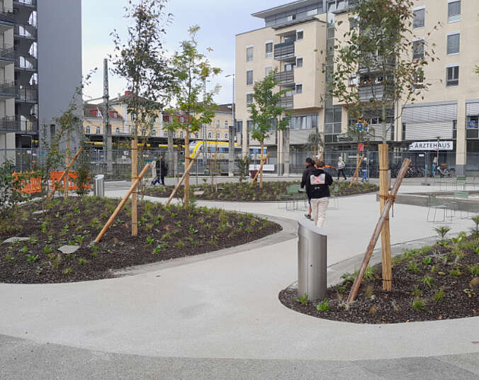 Bäume, Pflanzbeete und Wege, im Hintergrund Gebäude