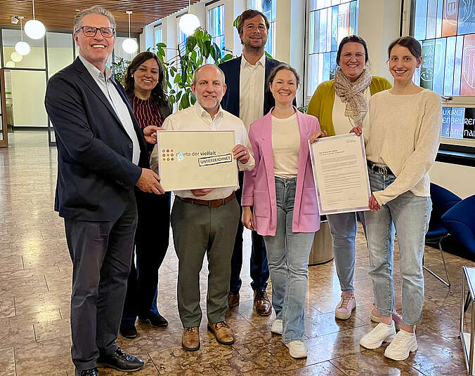 Gruppenbild mit Frauen und Männern, die Bild und Schriftstück halten