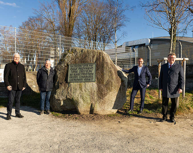 Vier Männer stehen vor einem großen Stein.