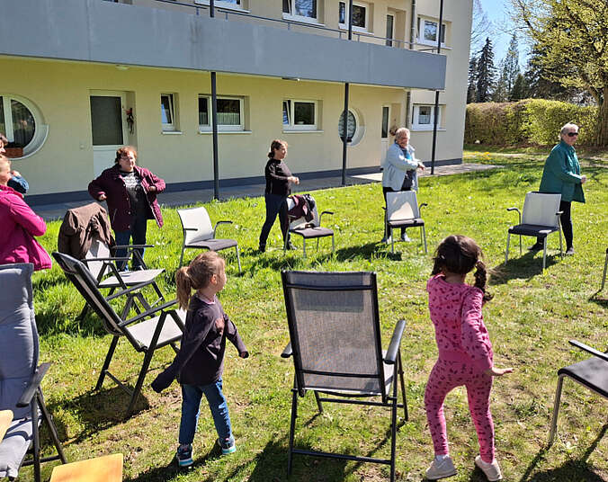 Kinder, Frauen und Männer auf einer Wiese die sich bewegen